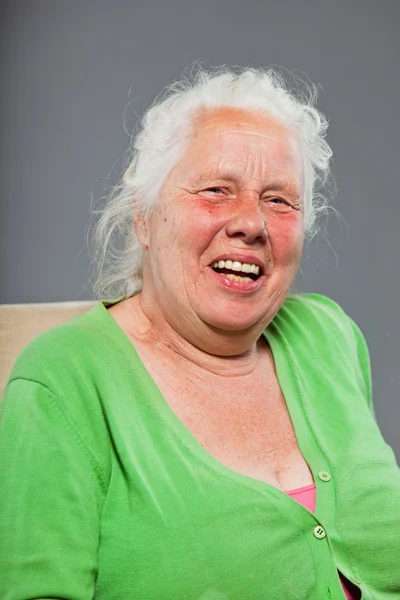 Glücklich entspannte Seniorin mit grauen langen Haaren im Stuhl sitzend. Studioaufnahme isoliert auf grauem Hintergrund. — Stockfoto