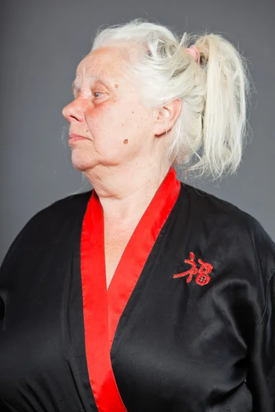 Starší žena s dlouhé šedivé vlasy, na sobě černé a červené kimono. Studio záběr izolované na šedém pozadí. — Stock fotografie