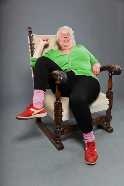 Szczęśliwy, zrelaksowany starszy kobieta z siwe włosy długo siedzi w fotelu. Studio strzał na białym tle na szarym tle. — Zdjęcie stockowe