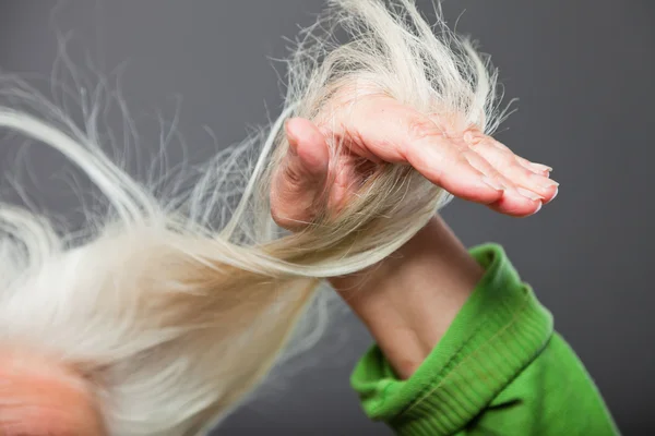 Close-up de mão de mulher sênior em cabelo. Tiro no estúdio. Isolado em cinza . — Fotografia de Stock