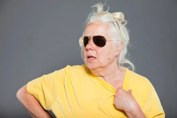 Mujer mayor de cadera fresca con gafas de sol y pelo largo y gris. Cara expresiva. Estudio de tiro aislado en gris . — Foto de Stock