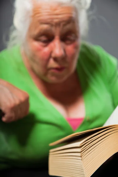Äldre kvinna sittande ordförande läser en bok. grå långt hår. Studio skott isolerade på grå bakgrund. — Stockfoto
