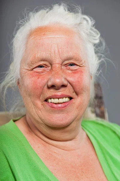 Щаслива розслаблена старша жінка з сірим довгим волоссям, що сидить у кріслі. Студійний знімок ізольовано на сірому фоні . — стокове фото