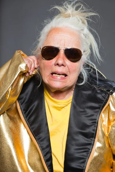 Cool senior woman wearing golden jacket. Long grey hair. Sunglasses. Studio shot. Isolated. — Stock Photo, Image