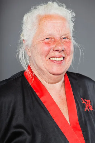 Старша жінка з довгим сірим волоссям в чорно-червоному кімоно. Студійний знімок ізольовано на сірому фоні . — стокове фото