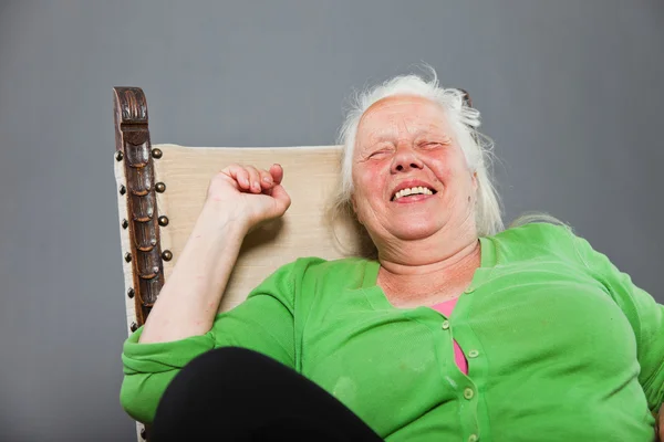 Mulher sênior relaxado feliz com cabelos longos cinza sentado na cadeira. Estúdio tiro isolado em fundo cinza . — Fotografia de Stock