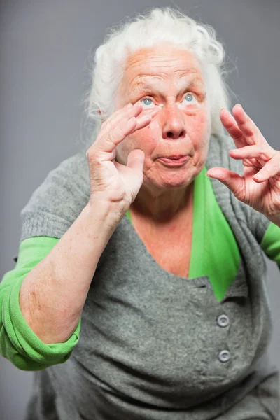 Mulher idosa expressiva engraçada. A agir jovem. Estúdio tiro isolado em fundo cinza . — Fotografia de Stock