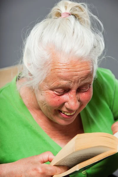 年配の女性の座っている椅子本を読んでします。灰色の長い髪。スタジオ撮影に分離の灰色の背景. — ストック写真
