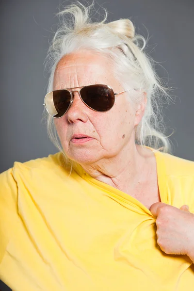 Cool hip senior femme avec des lunettes de soleil et de longs cheveux gris. Visage expressif. Studio tourné isolé sur gris . — Photo