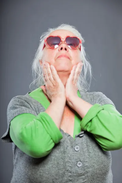 Donna anziana con gli occhiali da sole che fa facce strane. Espressivo. Studio girato isolato su sfondo grigio . — Foto Stock
