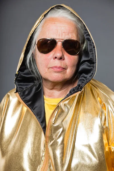 Cool starší žena nosí zlaté sako. dlouhé šedivé vlasy. sluneční brýle. Studio záběr. samostatný. — Stock fotografie
