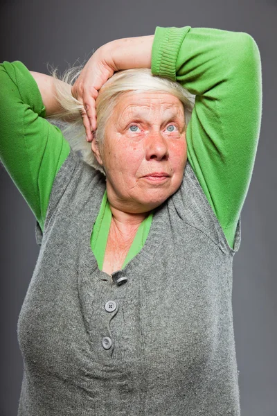 Senior vrouw houden handen in het haar. spirituele op zoek. studio opname geïsoleerd op grijze achtergrond. — Stockfoto