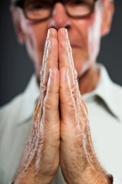 Expressive good looking senior man with glasses against grey wall. Hands praying. Spiritual and characteristic. Well dressed. Studio shot. — Stock Photo, Image