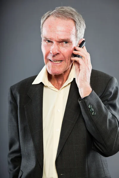Ausdrucksstarker gut aussehender älterer Herr im dunklen Anzug gegen graue Wand. Telefonieren mit dem Handy. Witzig und charakteristisch. Gut angezogen. Studioaufnahme. — Stockfoto