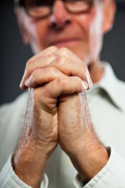 Uttrycksfulla bra söker äldre man med glasögon mot grå vägg. händerna bedjande. andliga och karakteristiska. välklädd. Studio skott. — Stockfoto
