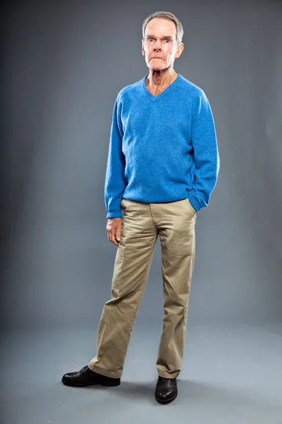 Expressive good looking senior man against grey wall. Funny and characteristic. Well dressed. Blue sweater. Studio shot. — Stock Photo, Image