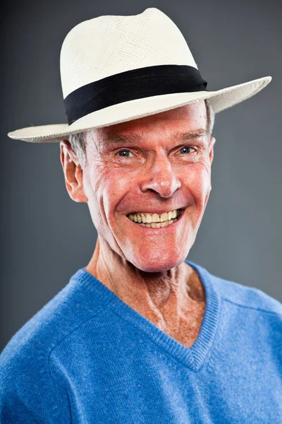 Выразительный симпатичный пожилой человек против серой стены. В шляпе. Забавно и характерно. Хорошо одет. Голубой свитер. Снимок студии . — стоковое фото