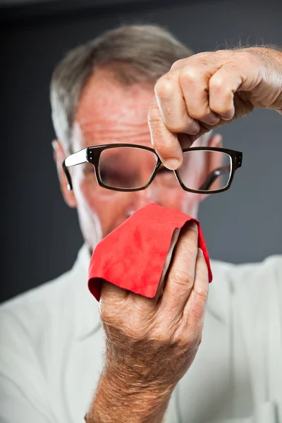 Ausdrucksstarker gut aussehender älterer Herr gegen graue Wand. Reinigung seiner Brille. Witzig und charakteristisch. Gut angezogen. Studioaufnahme. — Stockfoto