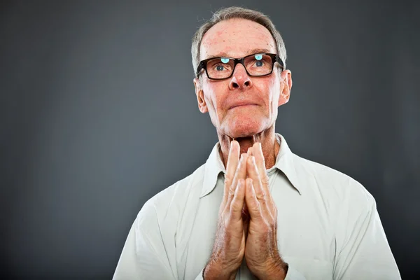 Expressive good looking senior man with glasses against grey wall. Hands praying. Spiritual and characteristic. Well dressed. Studio shot. — Stock Photo, Image