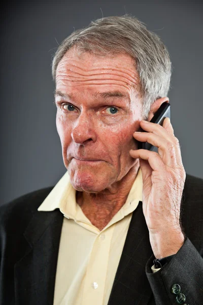Expressive good looking senior man in dark suit against grey wall. Calling with cell phone. Funny and characteristic. Well dressed. Studio shot. — Stock Photo, Image