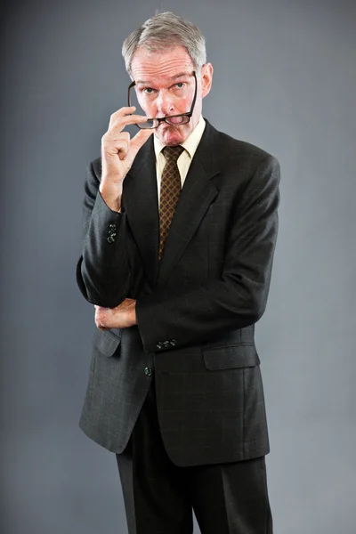 Εκφραστική καλή αναζητούν ανώτερος άνθρωπος σε σκούρο κοστούμι γκρι τοίχο. φορώντας γυαλιά. αστείο και χαρακτηριστικό. καλά ντυμένος. Studio που γυρίστηκε. — Φωτογραφία Αρχείου