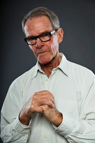 Espressivo bell'uomo anziano con gli occhiali contro la parete grigia. Mani in preghiera. Spirituale e caratteristico. Ben vestita. Studio girato . — Foto Stock