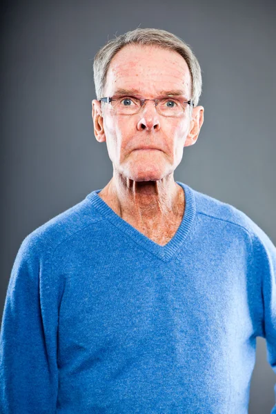 Ausdrucksstarker gut aussehender älterer Herr gegen graue Wand. Witzig und charakteristisch. Gut angezogen. blauer Pullover. Studioaufnahme. — Stockfoto