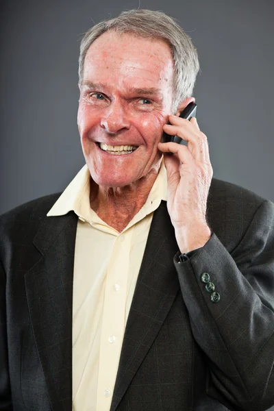 Espressivo bell'uomo anziano in abito scuro contro il muro grigio. Chiamo con il cellulare. Divertente e caratteristico. Ben vestita. Studio girato . — Foto Stock