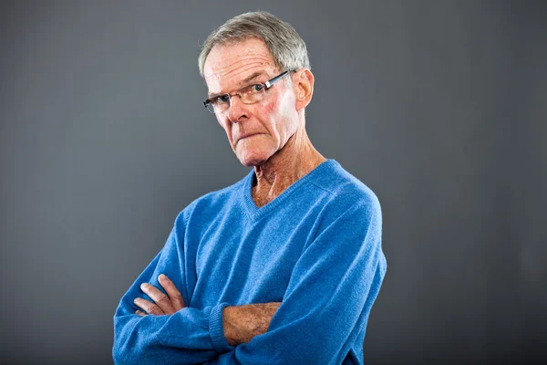 Expressieve goed uitziende senior man tegen grijs muur. grappig en karakteristiek. goed gekleed. blauwe trui. studio opname. — Stockfoto