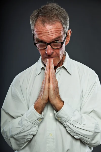 Ausdrucksstarker gut aussehender älterer Herr mit Brille vor grauer Wand. Hände beten. spirituell und charakteristisch. Gut angezogen. Studioaufnahme. — Stockfoto
