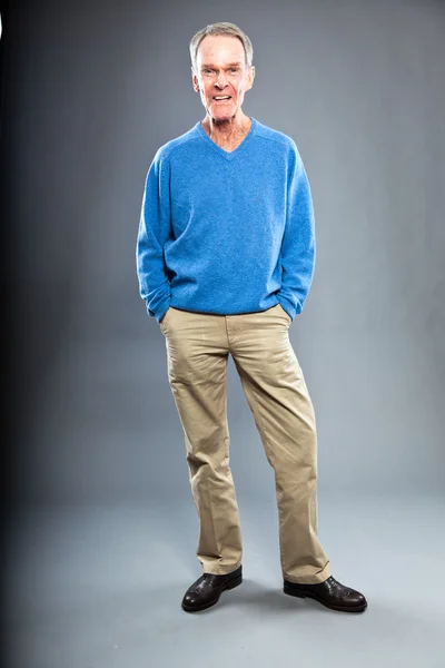 Expressive good looking senior man against grey wall. Funny and characteristic. Well dressed. Blue sweater. Studio shot. — Stock Photo, Image