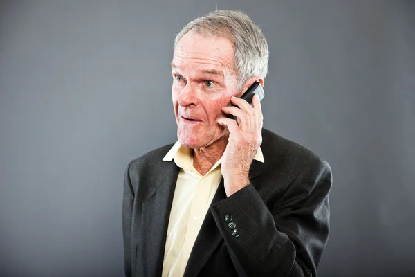 Expressive good looking senior man in dark suit against grey wall. Calling with cell phone. Funny and characteristic. Well dressed. Studio shot. — Stock Photo, Image