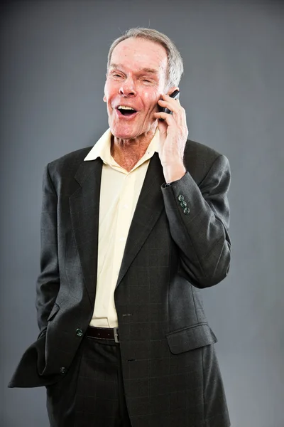 Uttrycksfulla snygg äldre man i mörk kostym mot grå vägg. ringa med mobiltelefon. rolig och karakteristiska. välklädd. Studio skott. — Stockfoto