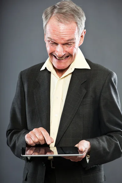 Homem sênior de boa aparência expressiva em terno escuro contra a parede cinza. Usando tablet. Engraçado e característico. Bem vestida. Estúdio . — Fotografia de Stock