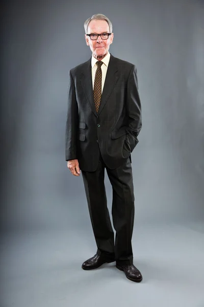 Expresivní dobře vypadající starší muž v tmavý oblek proti šedé zdi. nošení brýlí. zábavný a charakteristické. dobře oblečený. Studio záběr. — Stock fotografie