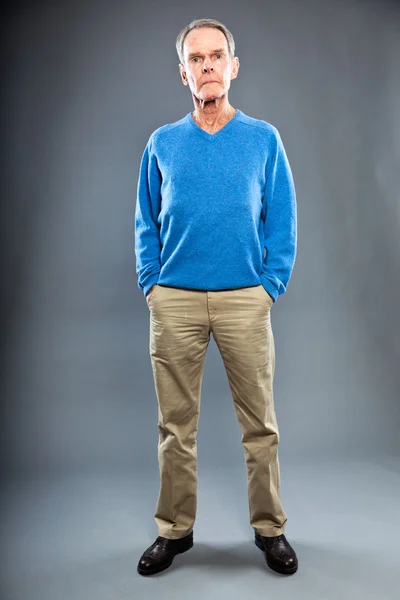 Hombre mayor expresivo y bien parecido contra la pared gris. Gracioso y característico. Bien vestido. Jersey azul. Captura de estudio . — Foto de Stock
