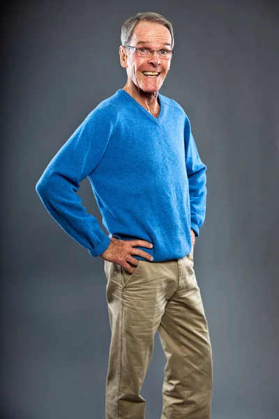 Hombre mayor expresivo y bien parecido contra la pared gris. Gracioso y característico. Bien vestido. Jersey azul. Captura de estudio . —  Fotos de Stock