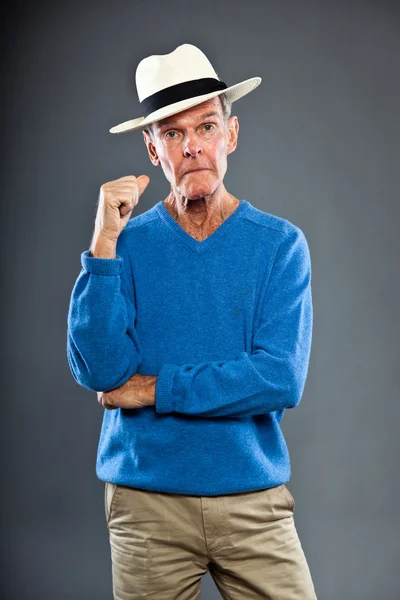Выразительный симпатичный пожилой человек против серой стены. В шляпе. Забавно и характерно. Хорошо одет. Голубой свитер. Снимок студии . — стоковое фото