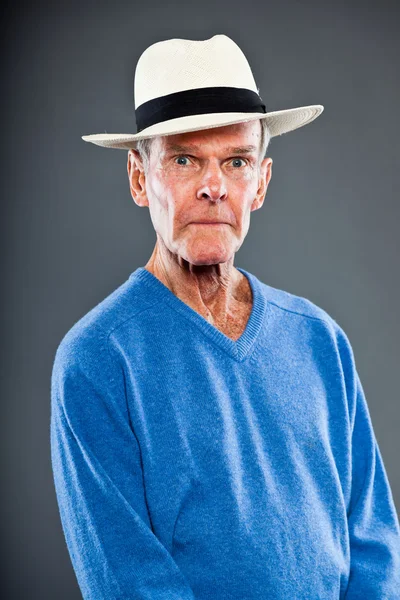 Expressieve goed uitziende senior man tegen grijs muur. het dragen van hoed. grappig en karakteristiek. goed gekleed. blauwe trui. studio opname. — Stockfoto