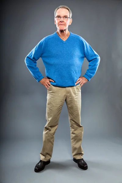 Expressieve goed uitziende senior man tegen grijs muur. grappig en karakteristiek. goed gekleed. blauwe trui. studio opname. — Stockfoto