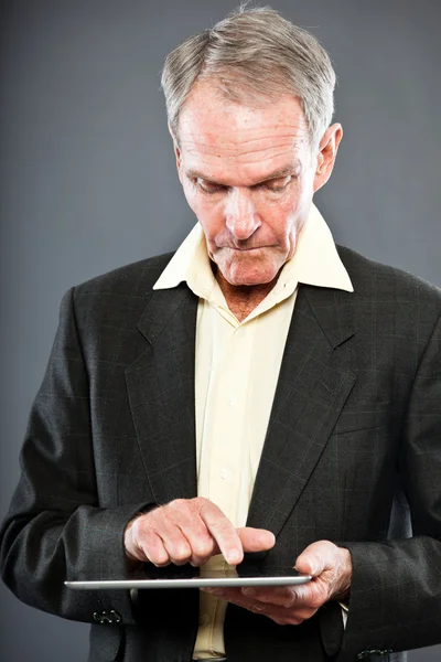 Ausdrucksstarker gut aussehender älterer Herr im dunklen Anzug gegen graue Wand. Tabletten verwenden. Witzig und charakteristisch. Gut angezogen. Studioaufnahme. — Stockfoto