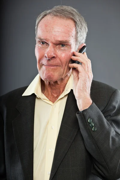 Uttrycksfulla snygg äldre man i mörk kostym mot grå vägg. ringa med mobiltelefon. rolig och karakteristiska. välklädd. Studio skott. — Stockfoto