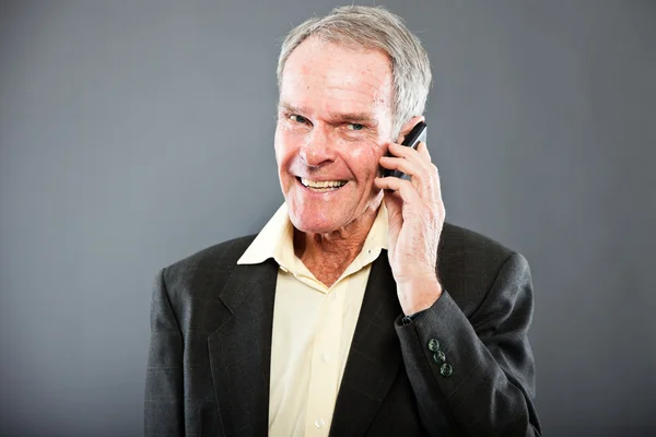 Expresivní dobře vypadající starší muž v tmavý oblek proti šedé zdi. volání s mobil. zábavný a charakteristické. dobře oblečený. Studio záběr. — Stock fotografie