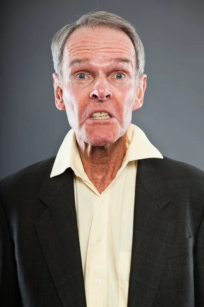 Ausdrucksstarker gut aussehender älterer Herr im dunklen Anzug gegen graue Wand. Witzig und charakteristisch. Gut angezogen. Studioaufnahme. — Stockfoto