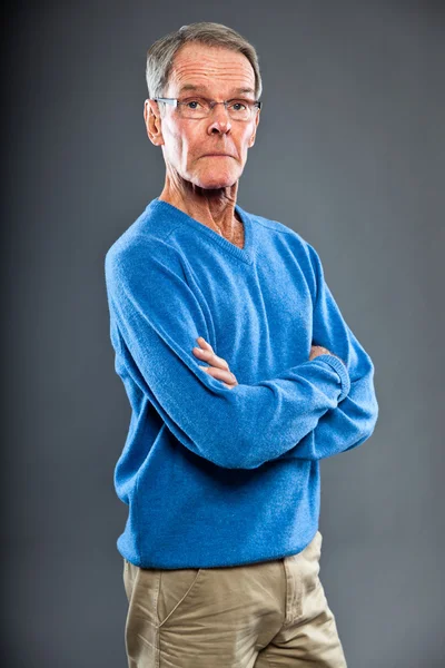 Ausdrucksstarker gut aussehender älterer Herr gegen graue Wand. Witzig und charakteristisch. Gut angezogen. blauer Pullover. Studioaufnahme. — Stockfoto