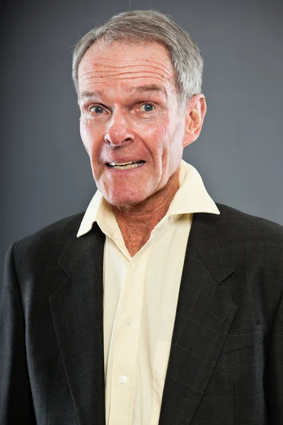 Expressieve goed uitziende senior man in donker pak tegen grijs muur. grappig en karakteristiek. goed gekleed. studio opname. — Stockfoto