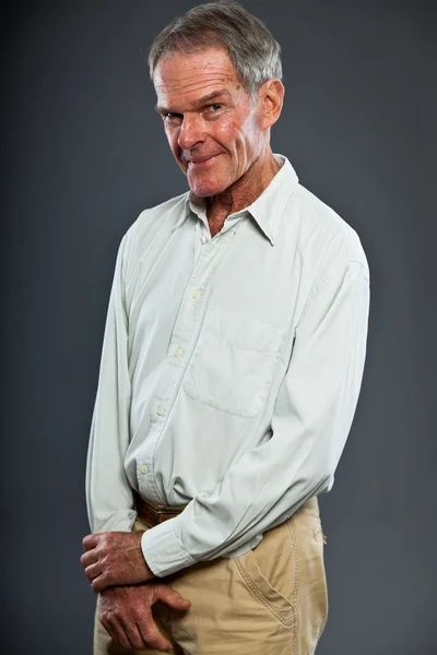 Kifejezően jóképű, idős ember a szürke falnál. Vicces és jellegzetes. Jól öltözött. Stúdió felvétel. — Stock Fotó