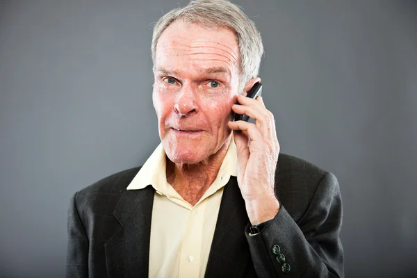Espressivo bell'uomo anziano in abito scuro contro il muro grigio. Chiamo con il cellulare. Divertente e caratteristico. Ben vestita. Studio girato . — Foto Stock