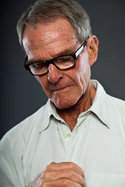 Expressieve goed uitziende senior man met bril tegen grijs muur. handen bidden. geestelijke en karakteristieke. goed gekleed. studio opname. — Stockfoto