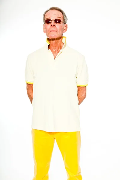 Выразительный, хорошо выглядящий пожилой мужчина, одетый в летнее платье, прислонившееся к белой стене. В солнечных очках. Счастливый, забавный и характерный. Изолирована. Снимок студии . — стоковое фото
